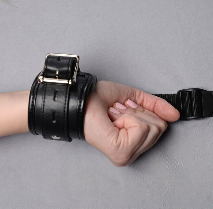 Close-up of a wrist secured in a padded restraint cuff with adjustable buckle and connected restraint strap