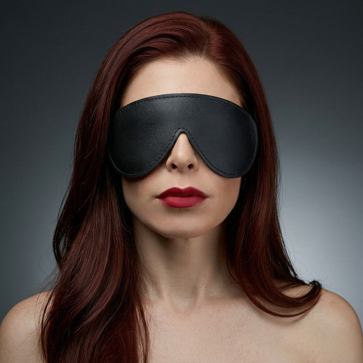 Female model wearing the Strict Leather padded blindfold with a smooth black finish and contoured design for complete light blockage and comfortable wear