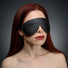 Female model wearing the Strict Leather padded blindfold shown from an angled view, highlighting the contoured shape and secure elastic strap