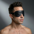 Male model wearing the Strict Leather padded blindfold from a side angle, showcasing the smooth black exterior and comfortable fit